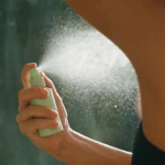 Close-up of a hand spraying a mist from a light green spray bottle outdoors.