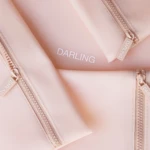 Close-up of a pale pink bag fabric with multiple pink zippers and 'DARLING' zipper pulls.