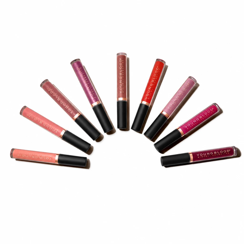 Assorted Youngblood lip gloss tubes arranged in a curved arc on a white background, showing various pinks, reds, and nudes.