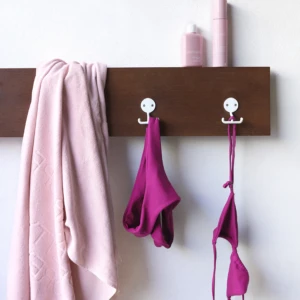 Pink towel and pink garments hanging on a brown wooden wall rack with two pink bottles on top.
