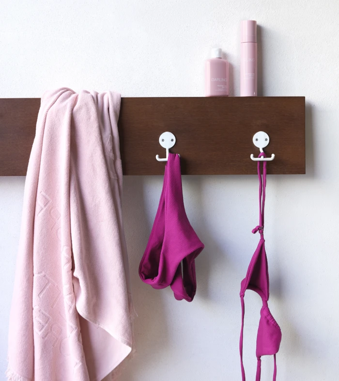 Pink towel and pink garments hanging on a brown wooden wall rack with two pink bottles on top.