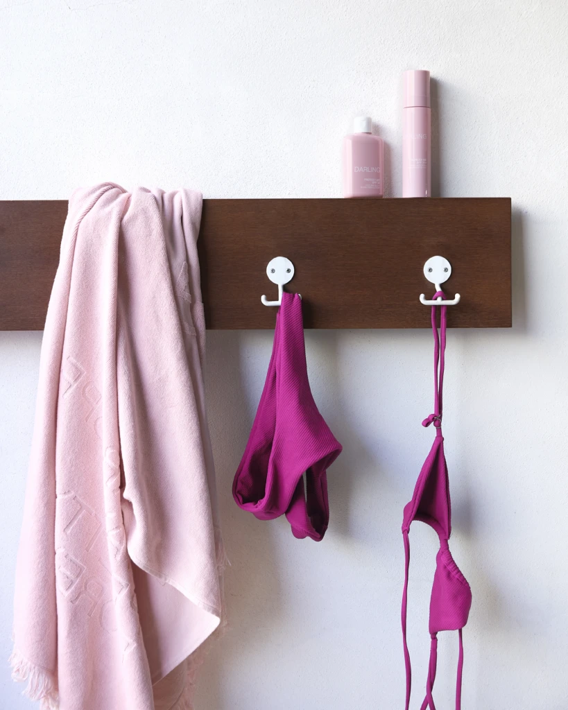 Pink towel and pink garments hanging on a brown wooden wall rack with two pink bottles on top.