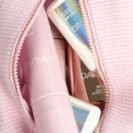 Open pink makeup bag showing pastel pink cosmetic tubes inside a textured zipper pouch with an iridescent card.