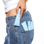 Person in blue jeans with light blue skincare tubes tucked into the back pocket.