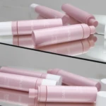 Pink cylindrical lip balm tubes arranged on a mirrored vanity surface with reflections visible.