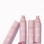 Row of pink Darling sunscreen spray bottles standing upright against a white background, with caps removed on some.