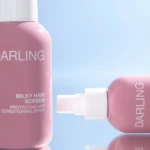 Close-up of a pink hair spray bottle with a white cap against a blue background.