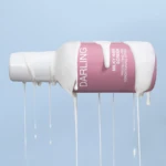 Close-up of a pink and white bottle tilted on a pale blue background, with dripping white liquid and the label reading 'DARKLING'.
