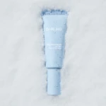 Blue Darling sunscreen tube half-buried in snow with water droplets on the label