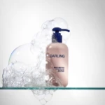 Close-up of a pink Darling body wash pump bottle with bubbles around the nozzle against a white background.