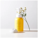 Yellow Real Green natural kids shampoo bottle with pump, foam on a white surface and a sprig of small yellow flowers beside it