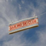 Striped towel with red text 'DARLING SKI CLUB' hanging on a clothesline against a blue sky.