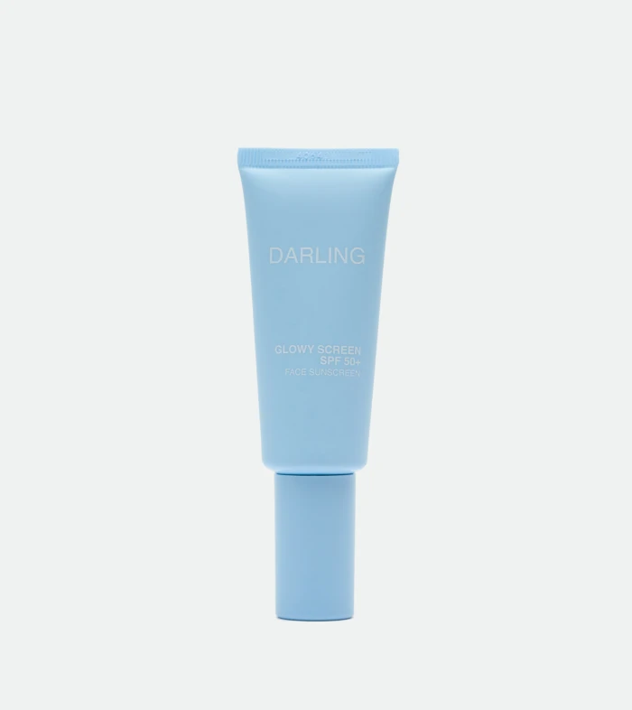 Blue sunscreen tube labeled 'DARLING' with SPF 50+ standing upright against a pale background, showing 'GLOWY SCREEN' text.