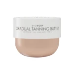 Close-up of a white cosmetic jar displaying the text 'BALI BODY GRADUAL TANNING BUTTER' with beige lotion visible at the bottom edge, indicating a tanning product.
