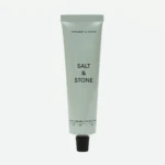 Tall gray squeeze tube of hand cream with black text, reading 'BERGAMOT & HINOKI' near the top and 'SALT & STONE' midsection, with a black cap at the bottom
