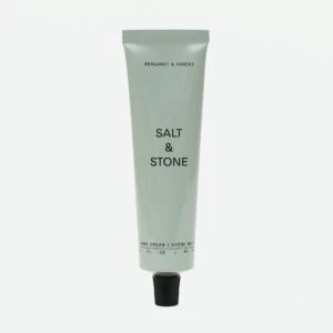 Tall gray squeeze tube of hand cream with black text, reading 'BERGAMOT & HINOKI' near the top and 'SALT & STONE' midsection, with a black cap at the bottom