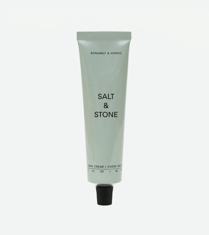 Tall gray squeeze tube of hand cream with black text, reading 'BERGAMOT & HINOKI' near the top and 'SALT & STONE' midsection, with a black cap at the bottom