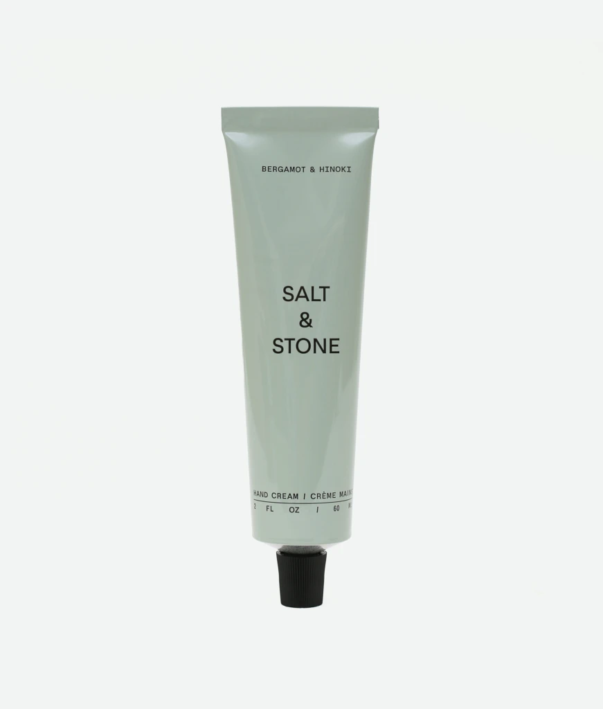 Tall gray squeeze tube of hand cream with black text, reading 'BERGAMOT & HINOKI' near the top and 'SALT & STONE' midsection, with a black cap at the bottom