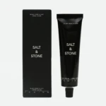 Black box and black squeeze tube of Salt & Stone hand cream with white text reading 'Black Rose & Oud' on a light background.