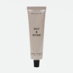 Beige Salt & Stone hand cream tube standing upright with a black cap at the bottom and visible brand text on the front.