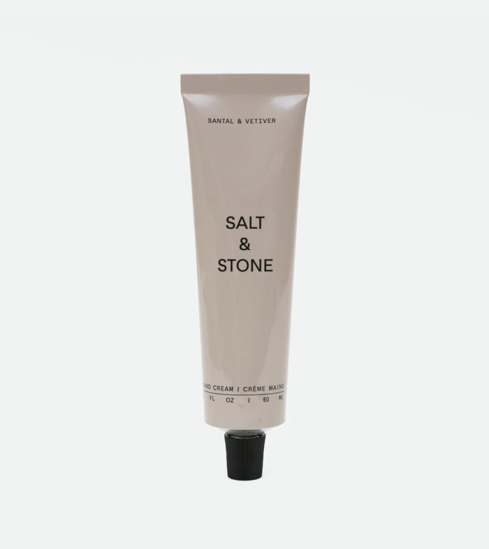 Beige Salt & Stone hand cream tube standing upright with a black cap at the bottom and visible brand text on the front.