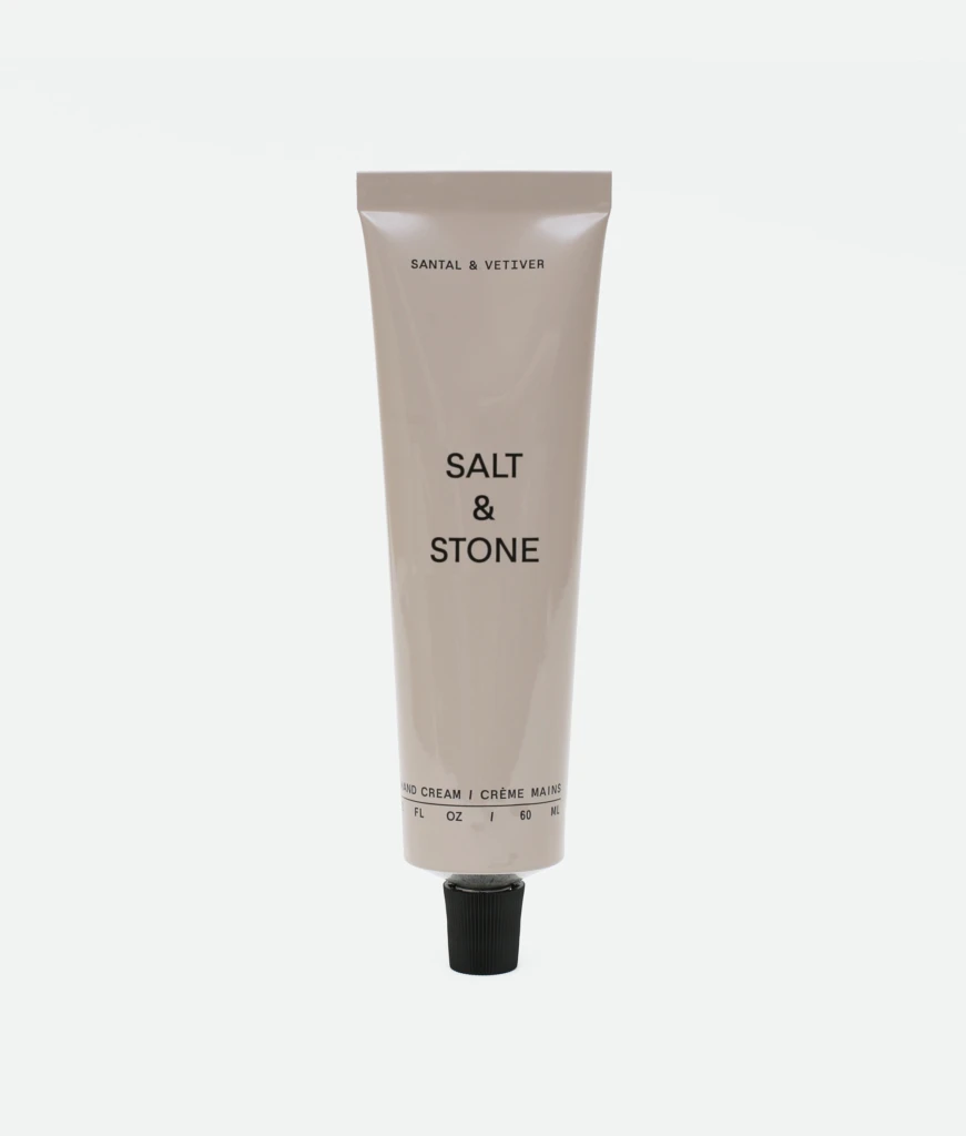 Beige Salt & Stone hand cream tube standing upright with a black cap at the bottom and visible brand text on the front.
