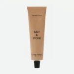 Beige squeeze tube of skincare labeled 'Saffron & Cedar' with 'Salt & Stone' brand, standing upright.