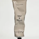 Beige squeeze tube labeled 'Salt & Stone' with 'Santal & Vetiver', standing upright on a pale background with a black cap.