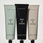 Three Salt & Stone body lotion tubes in pastel green, black, and beige with scents Bergamot & Hinoki, Black Rose & Oud, Santal & Vetiver.