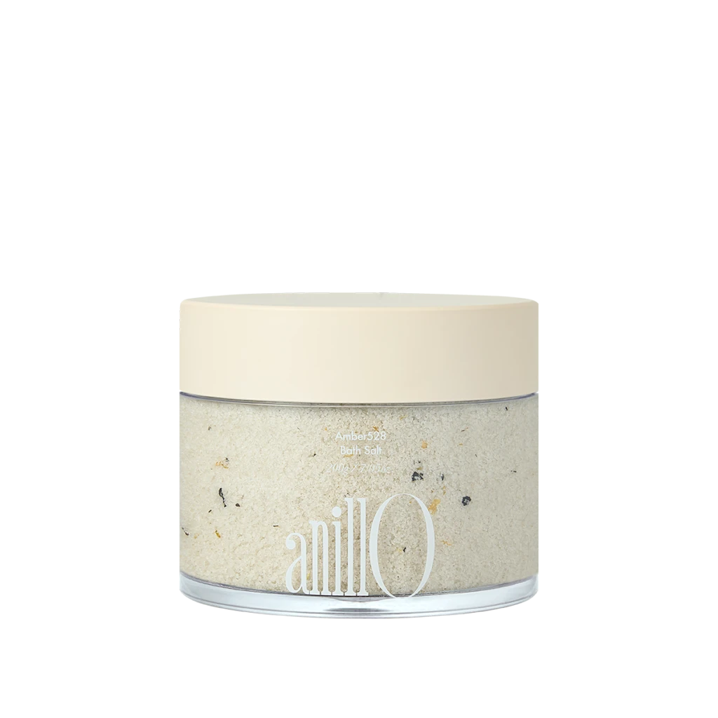 Cream-colored lid on a glass jar of bath salt with speckled crystals visible through the clear body; brand name 'anillo' on the label