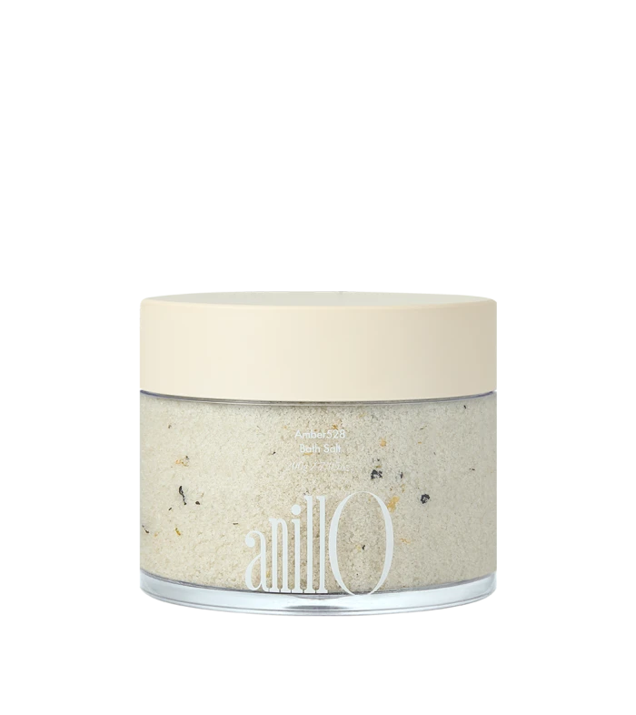Cream-colored lid on a glass jar of bath salt with speckled crystals visible through the clear body; brand name 'anillo' on the label