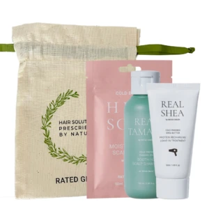 Beige fabric tote with green strap containing a hair care gift set: pink pouch, teal bottle, and white Real Shea tube.