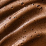 Close-up of brown bubbly foam with droplets on a smooth, textured surface (chocolatey or coffee foam).