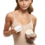 Woman in a beige bodysuit holding a jar of cream in each hand, showcasing skincare product Balbody.