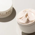 Open white jar of creamy moisturizer on a pale surface, with the lid labeled 'BALIBODY' beside it, a skincare product.