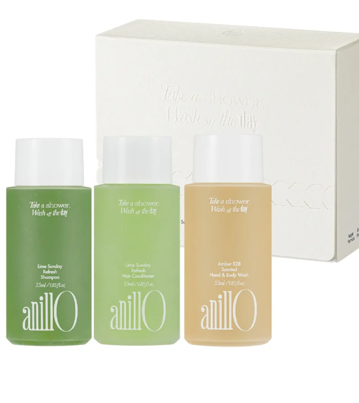 Three travel-size Anillo personal care bottles (shampoo, conditioner, hand & body wash) in green and amber hues with a white box behind them.