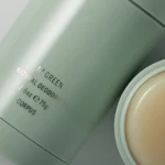 Close-up of a green cosmetic jar with a beige lid and partial text reading 'Natural Deodorant'.