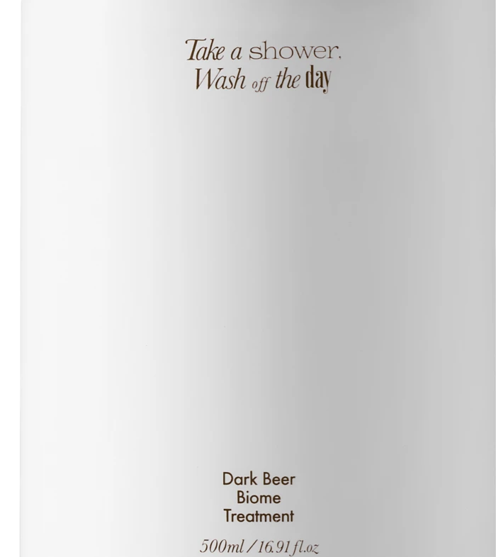 White pump bottle with a black nozzle, featuring brown text: 'Take a shower, Wash off the day' and 'Dark Beer Biome Treatment' 500 ml.