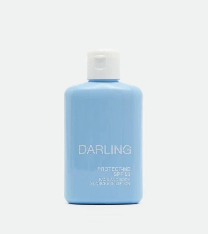 Close-up of a light blue sunscreen bottle with a white flip-top cap, showing the label 'DARLING' and 'PROTECT-ME SPF 50'.