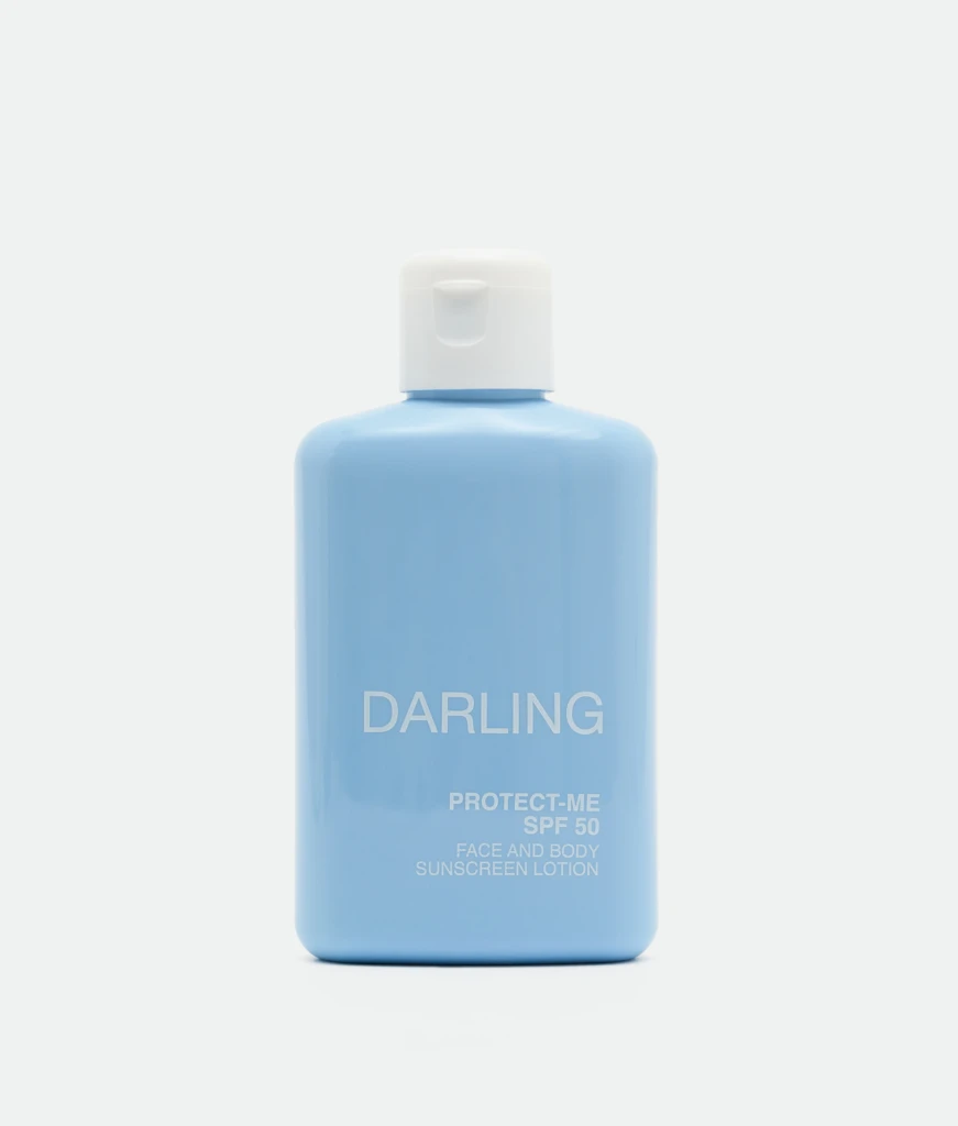 Close-up of a light blue sunscreen bottle with a white flip-top cap, showing the label 'DARLING' and 'PROTECT-ME SPF 50'.