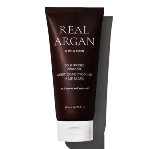 Dark brown tube of Real Arg an by Rated Green, labeled Cold Pressed Argan Oil Deep Conditioning Hair Mask with 200 ml capacity, shown against a black background with white stripes behind.