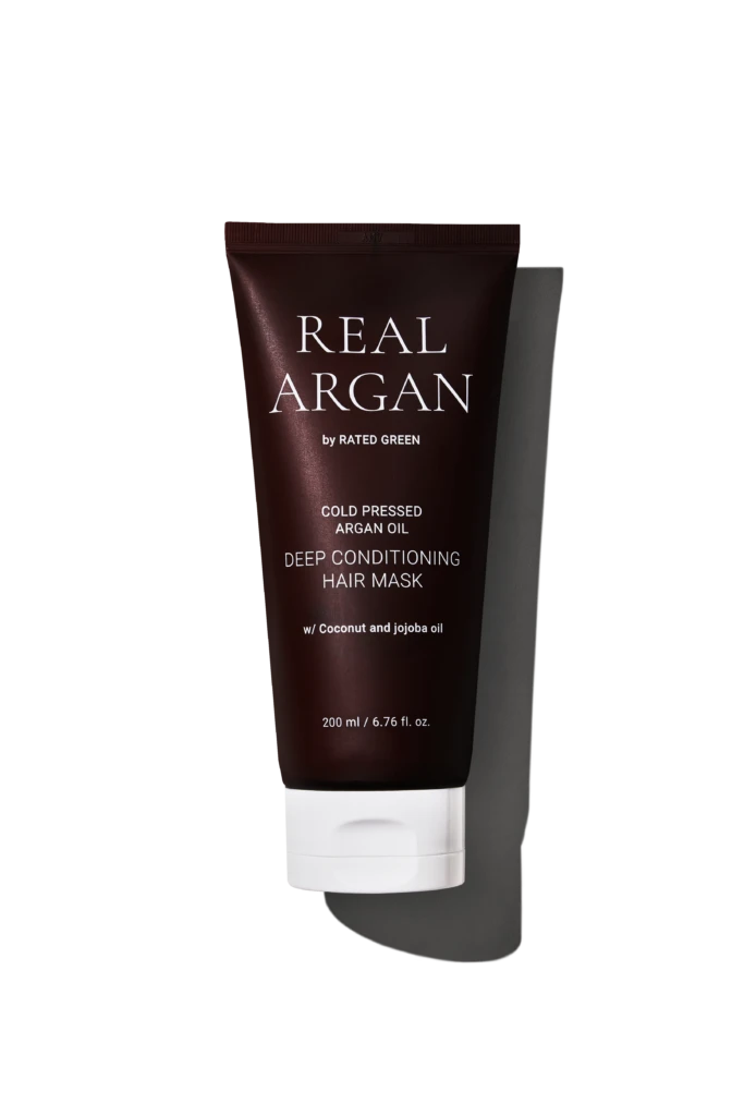 Dark brown tube of Real Arg an by Rated Green, labeled Cold Pressed Argan Oil Deep Conditioning Hair Mask with 200 ml capacity, shown against a black background with white stripes behind.