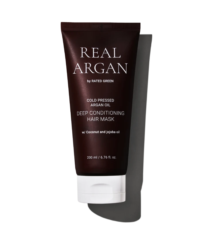 Dark brown tube of Real Arg an by Rated Green, labeled Cold Pressed Argan Oil Deep Conditioning Hair Mask with 200 ml capacity, shown against a black background with white stripes behind.