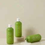 Green Real Mary shampoo bottles on a neutral backdrop, with one bottle tipped and spilling product onto the surface.