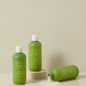 Green Real Mary shampoo bottles on a neutral backdrop, with one bottle tipped and spilling product onto the surface.