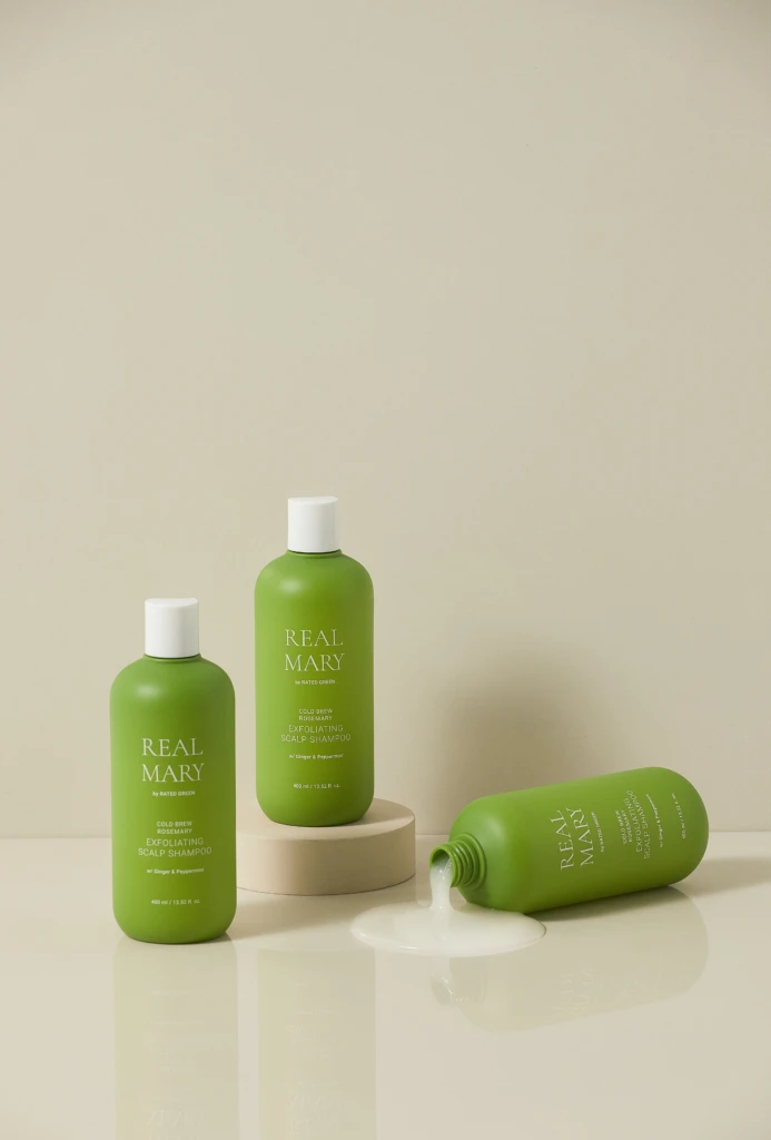 Green Real Mary shampoo bottles on a neutral backdrop, with one bottle tipped and spilling product onto the surface.