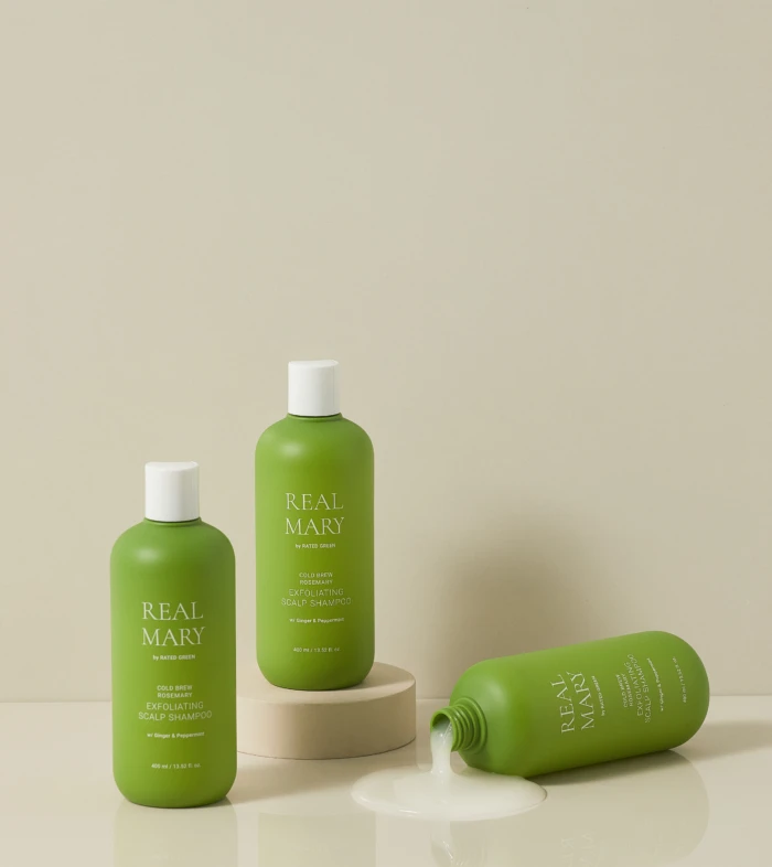 Green Real Mary shampoo bottles on a neutral backdrop, with one bottle tipped and spilling product onto the surface.