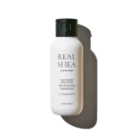 White shampoo bottle with black flip cap, label reads 'REAL SHEA' and 'NOURISHING SHAMPOO' (Sunflower Seed Oil) - product shot against dark background