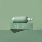 Green cosmetic dropper bottle resting on a matching green box, both with white text, against a pale green background.
