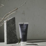 Tube of Real Grow anti-hair loss fortifying treatment on a wooden platform beside a stone block and dry branches.
